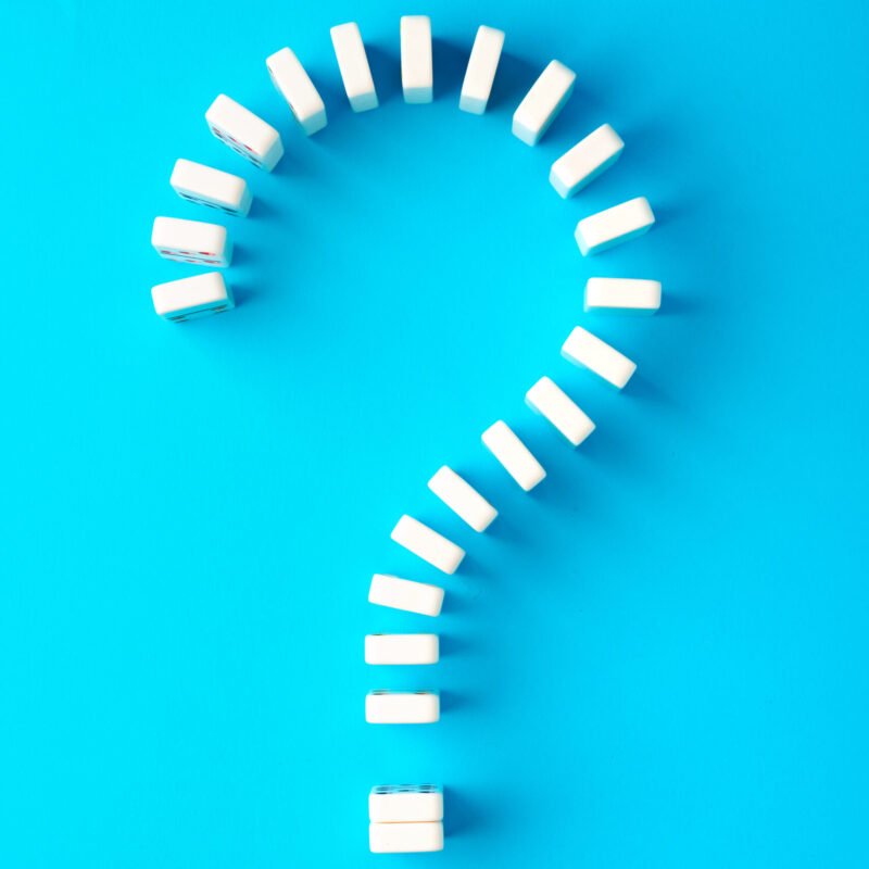 Domino tiles set in question sign shape on blue background top view